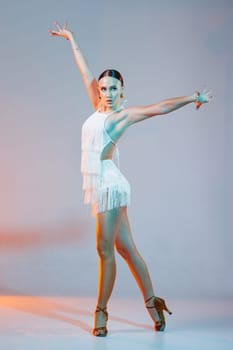Confident female Latin dancer posing in a fringe dress under dramatic orange-blue light on studio stage.