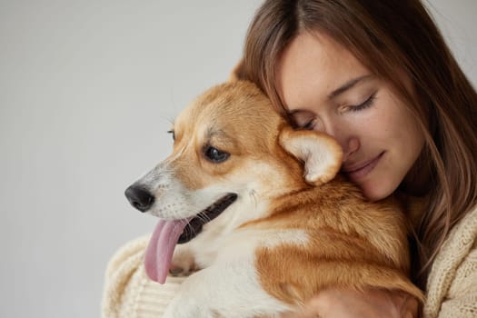 Young woman hugging adorable Corgi dog with closed eyes, feeling pure love, cozy emotional moment indoors.