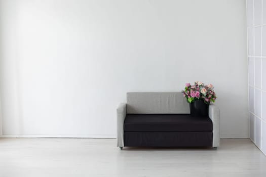 Gray office sofa with flowers and gifts in the interior of a white room with a window