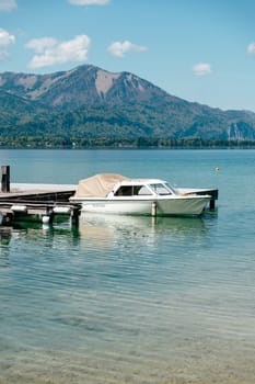 A boat rests at the dock of Wolfgangsee in Strobl, Upper Austria. Surrounded by mountains, the calm lake reflects the clear sky, capturing the essence of spring and summer relaxation.