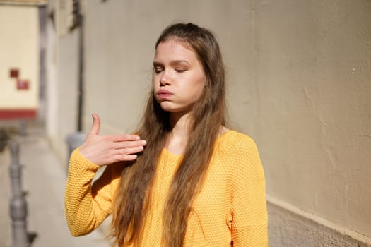 A young woman can be seen wearing a vibrant yellow sweater, posing thoughtfully against a textured wall, which showcases her unique creativity and deep introspection in a lively urban environment