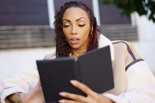 A focused woman is immersed in reading an ebook outdoors, perfectly showcasing a modern reading experience while dressed in a chic and stylish outfit that reflects her contemporary lifestyle