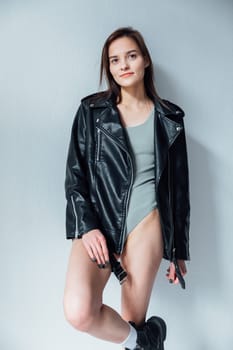 Portrait of a beautiful fashionable brunette woman in a leather jacket on a gray background