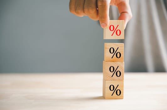 Concept of interest rate and mortgage rates. Hand positioning a wooden cube block that represents growth and an upward direction, accompanied by a percentage symbol.