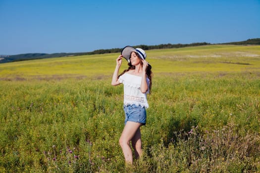 Woman in summer hat with brim smiling and walking in rural field in summer by road