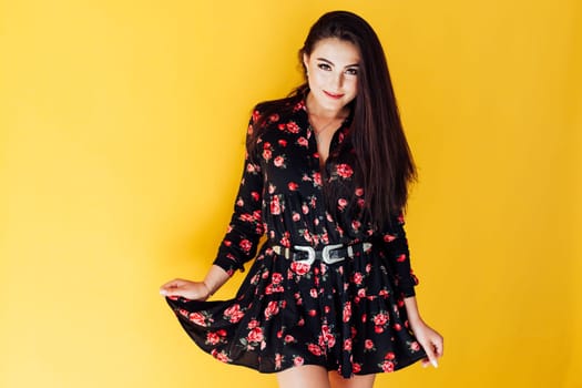 Brunette woman in black summer dress with flowers on yellow background