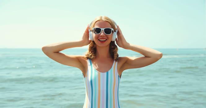 Summer vacation of happy young woman smiles enjoying listening to music with headphones, relaxed cheerful girl wearing a sunglasses on the beach at sea coast with blue sky on a sunny day