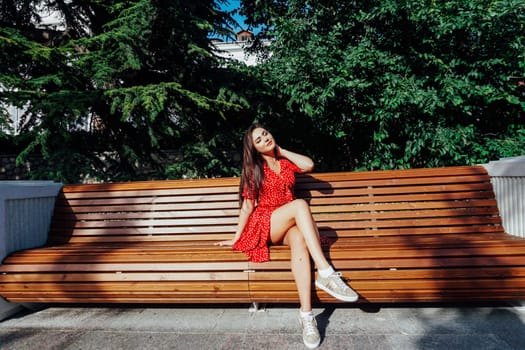 Brunette in a red polka dot dress in summer hanging out on a bench