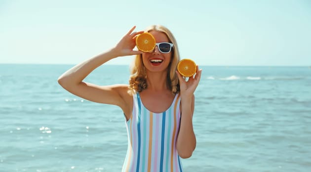 Summer vacation, portrait of happy smiling young woman, laughing, holding oranges fruits, having fun, wearing a swimsuit on the beach on sea coast background