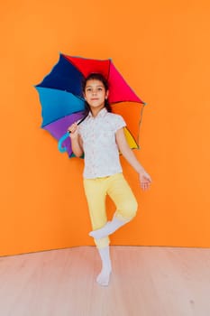Little girl with colorful rain umbrella on orange background