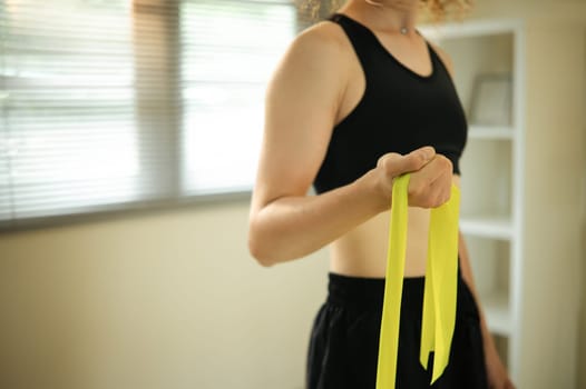 Active Russian woman using resistance band for arm exercises in a bright living room.