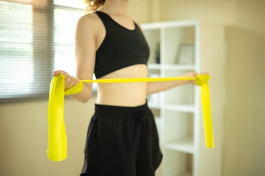 Active Russian woman using resistance band for arm exercises in a bright living room.