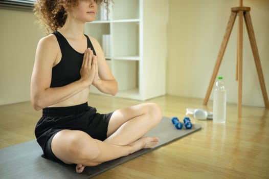 Young Russian woman with curly hair practicing yoga at home.