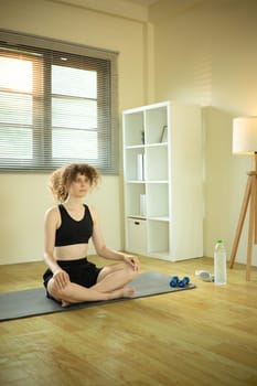 Young Russian woman with curly hair practicing yoga at home.