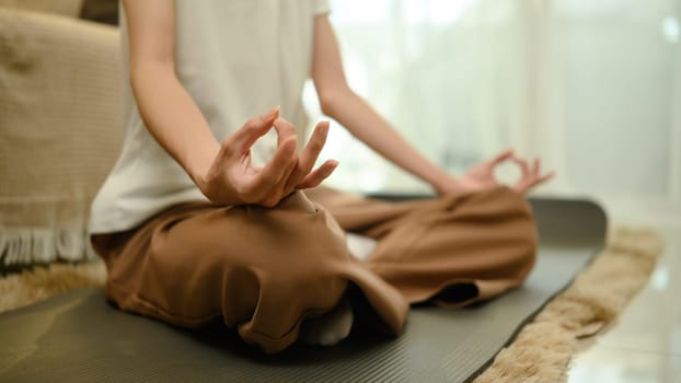 Close up of young man practicing meditation on mat at home.
