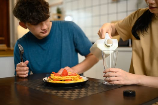 Young couple enjoying a breakfast together with pancakes and a glass of milk in home kitchen.