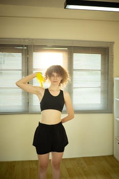 Active Russian woman using resistance band for arm exercises in a bright living room.