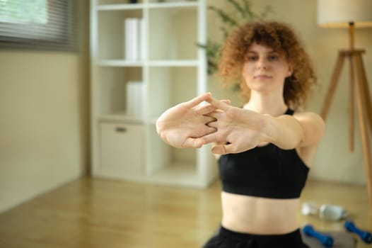 Fit young woman in sportswear doing arm stretches in a cozy home.
