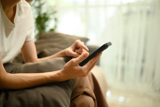 Close up of man using smartphone while relaxing on couch at home.