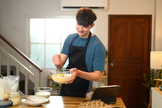Cheerful man blending ingredients for pancakes, creating a homemade breakfast.