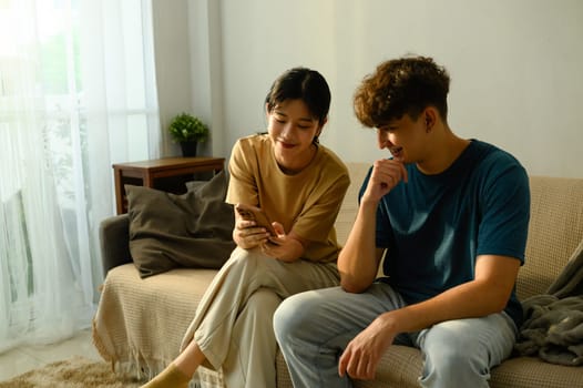 Relaxed couple sitting on couch together and looking at a mobile phone in a living room.