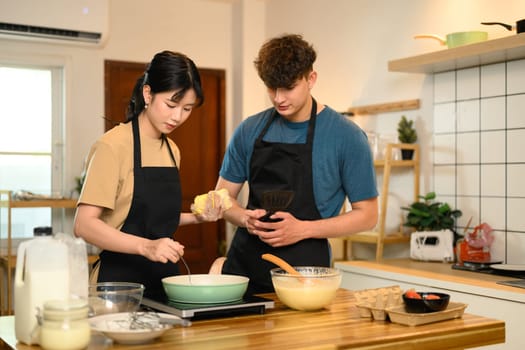 Couple enjoying morning cooking time, preparing pancake batter together in kitchen.