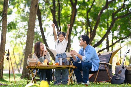 Happy family enjoying picnic and quality time together at a park with tents in the background.
