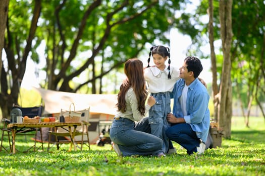 Happy family enjoying quality time together at a forest campsite with tents and picnic setup.