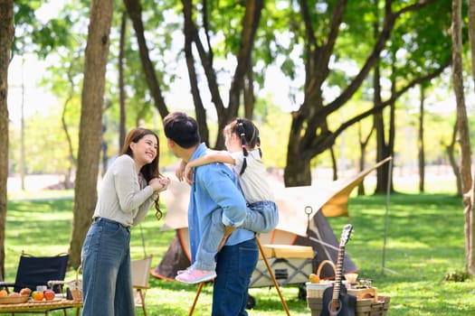Happy family enjoying quality time together at a forest campsite with tents and picnic setup.