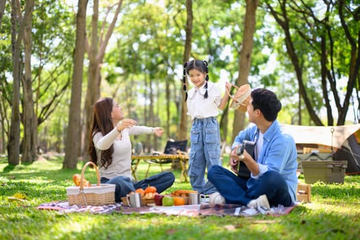 Cheerful family camping outdoors, sharing snacks and spending quality time near tent in the park..