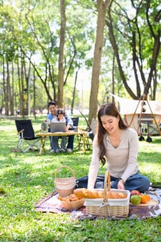 Woman arranging food for a picnic while her family enjoys time at a forest campsite.