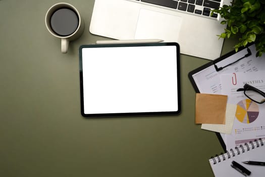 Digital tablet with blank screen surrounded by laptop, financial charts, and office supplies.
