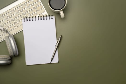 Modern workspace with headphones, coffee mug, and spiral notebook on green surface.