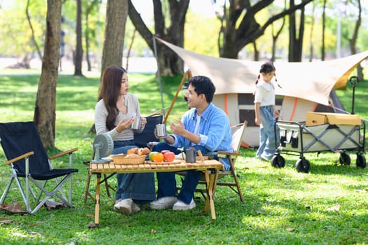 Cheerful parents enjoying a warm drink together at campsite.