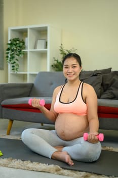Pregnant woman working out indoors with small dumbbells.