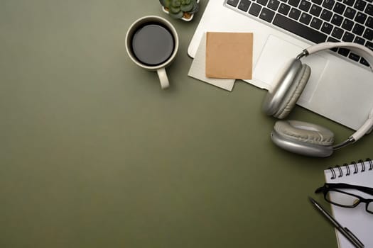 Flat lay of stylish desktop with laptop, coffee cup, headphones, and planner on green desk.