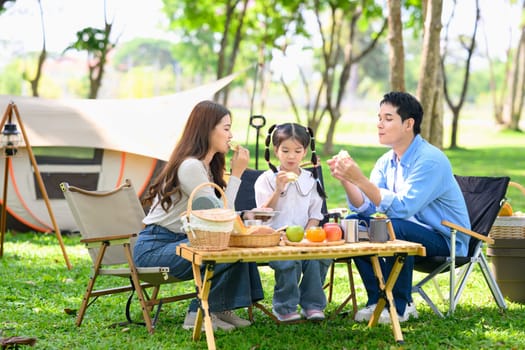 Cheerful family camping outdoors, sharing snacks and spending quality time near tent in the park..