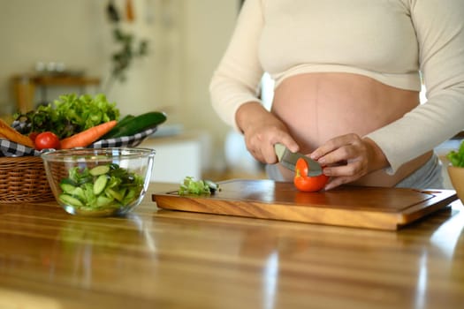Pregnant woman preparing a fresh vegetable salad in the kitchen.
