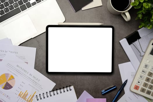 Digital tablet with blank screen surrounded by business documents, laptop, and calculator on office desk.