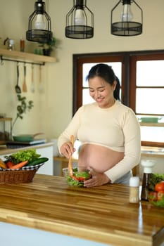 Pregnant woman preparing a fresh vegetable salad in the kitchen.