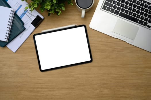 Top view of modern office desk with digital tablet, laptop, coffee cup, and notebook.