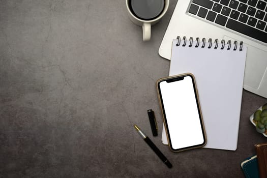 Smartphone with white screen on notepad next to a laptop on concrete style surface.