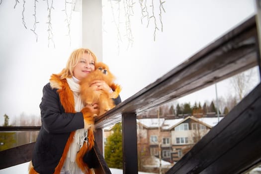 A woman lovingly holds her fluffy red Pomeranian while standing outdoors in a snow-covered area during winter.
