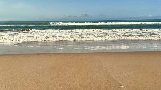 The stunning view features gentle ocean waves endlessly lapping at a beautiful sandy beach under a clear blue sky