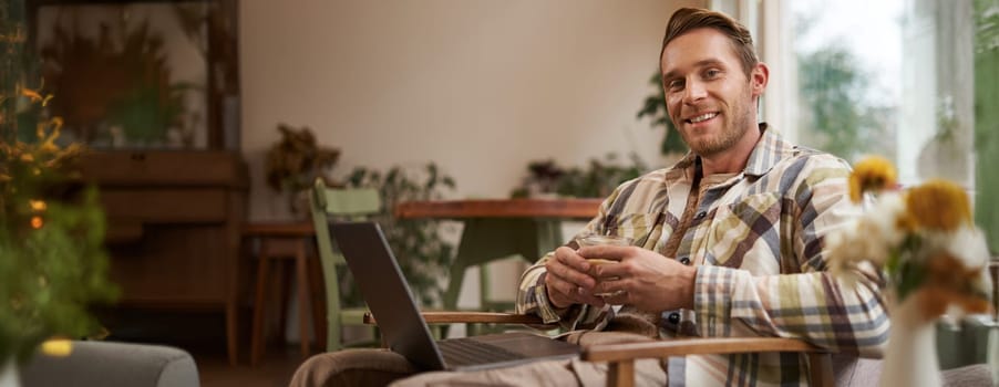 Handsome young professional, businessman sitting in cafe with glass of coffee and working on laptop, searching for inspiration outside of office workspace.