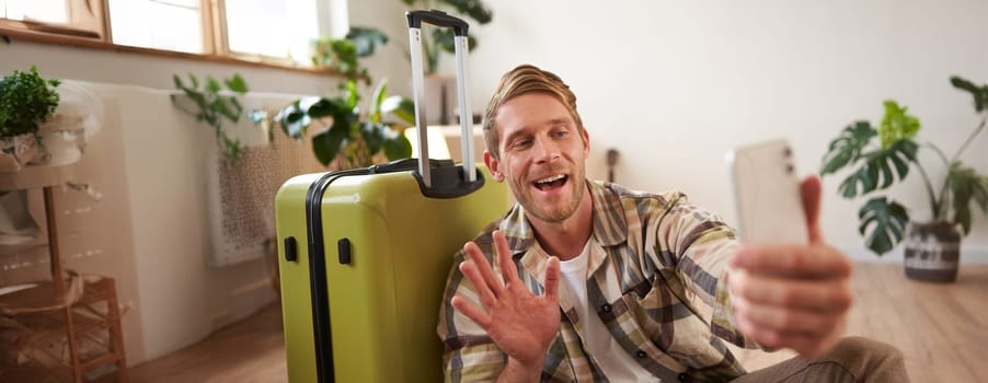 Lifestyle blogger takes photos with his suitcase, shows luggage, goes on holiday, makes selfies on mobile phone. Tourism concept