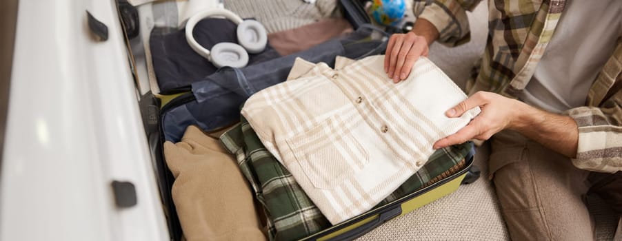 Cropped shot of male hands, tourist puts his clothes in suitcase, packs luggage for holiday trip, goes on vacation.