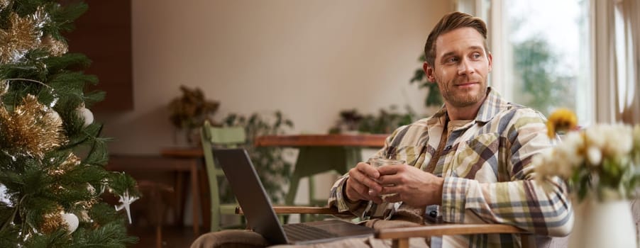 Handsome young professional, businessman sitting in cafe with glass of coffee and working on laptop, searching for inspiration outside of office workspace.