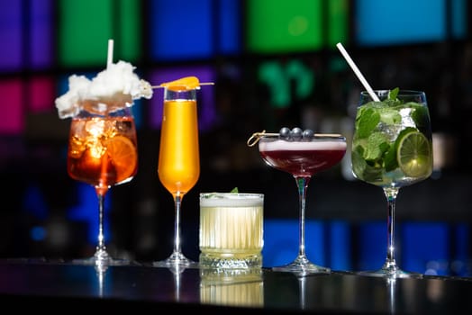 row of various colourfull alcoholic cocktails on a bar desk. Glasses of differen shapes on a fancy background
