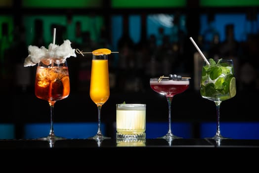 row of various colourfull alcoholic cocktails on a bar desk. Glasses of differen shapes on a fancy background